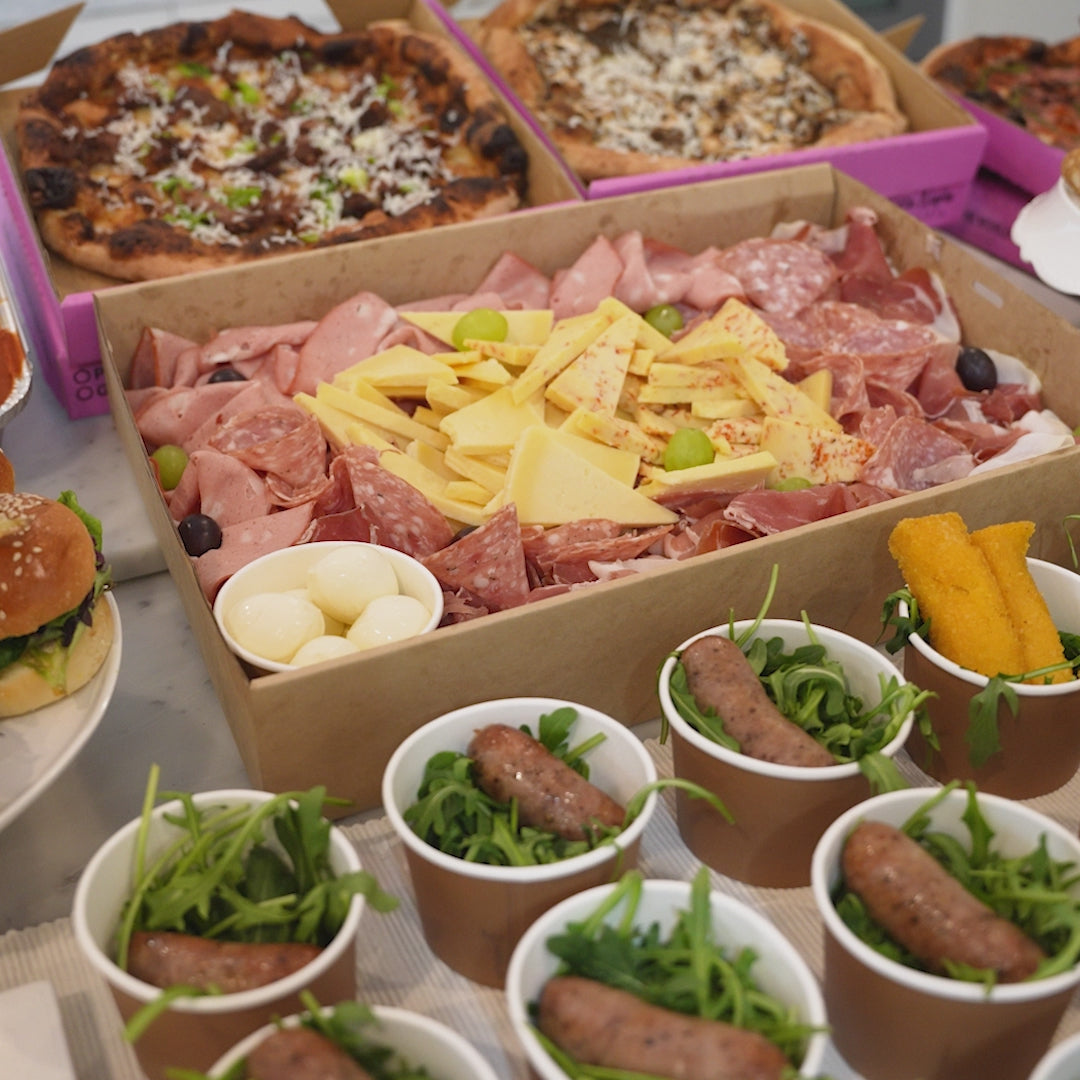 Pizza, sliders, arancini and a cured meat platter laid out on a table.
